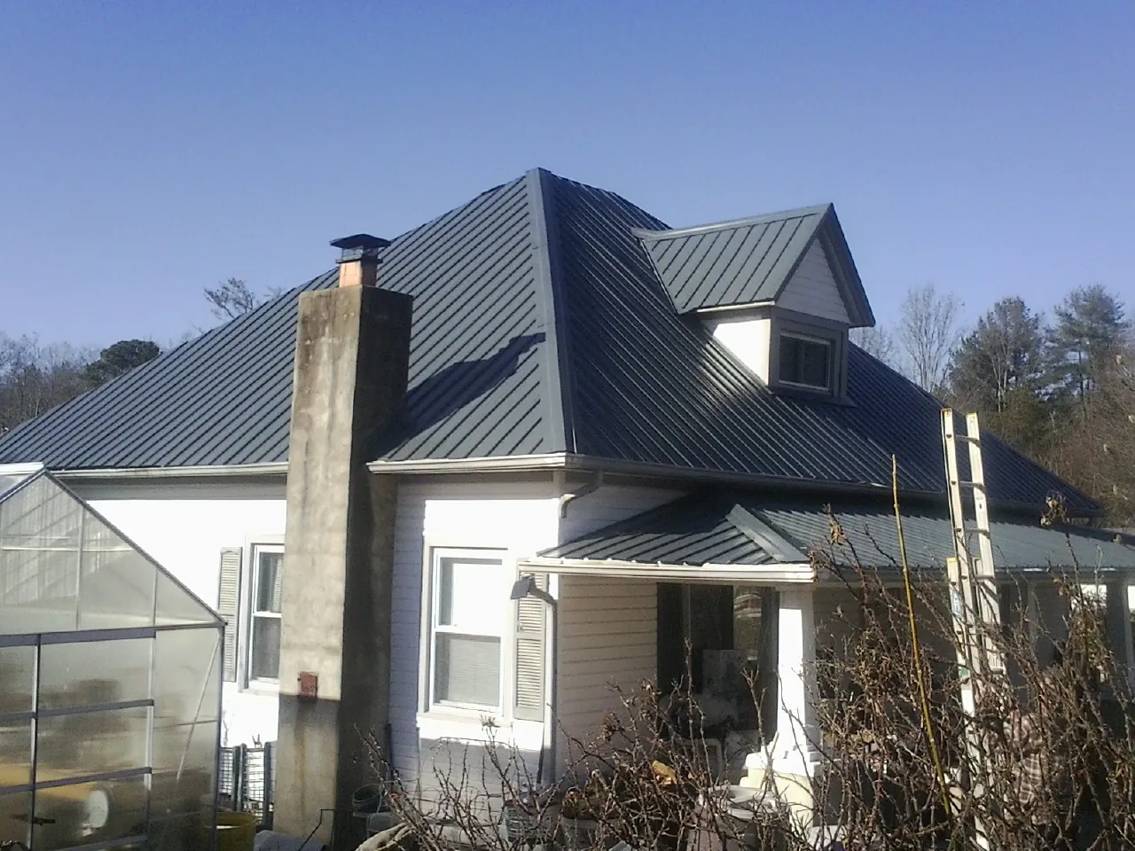 Dark blue standing seam metal roof on a white farmhouse with dormer — Slate & Tile Roof Repair by Roofing Brothers in Saint Bonifacius