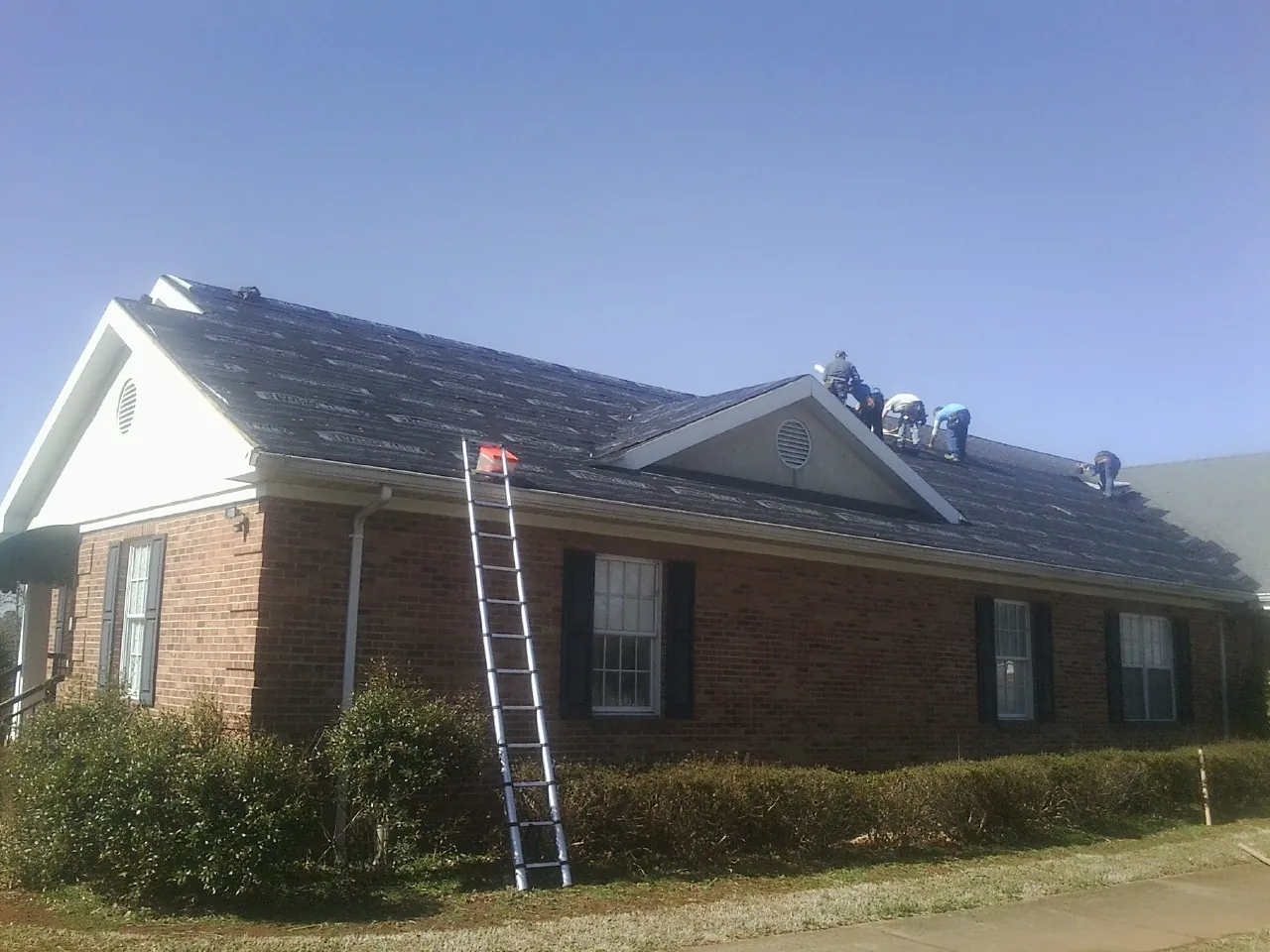Crew tearing shingles off a brick ranch roof with a ladder set — Emergency Roof Repair work by our crew in Saint Bonifacius
