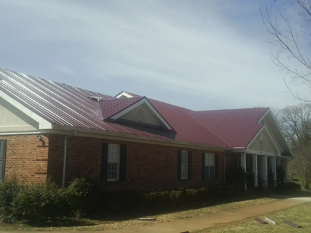 Red metal roof with gabled entries on a long brick building, from a Hail Damage Roof Repair job in Saint Bonifacius