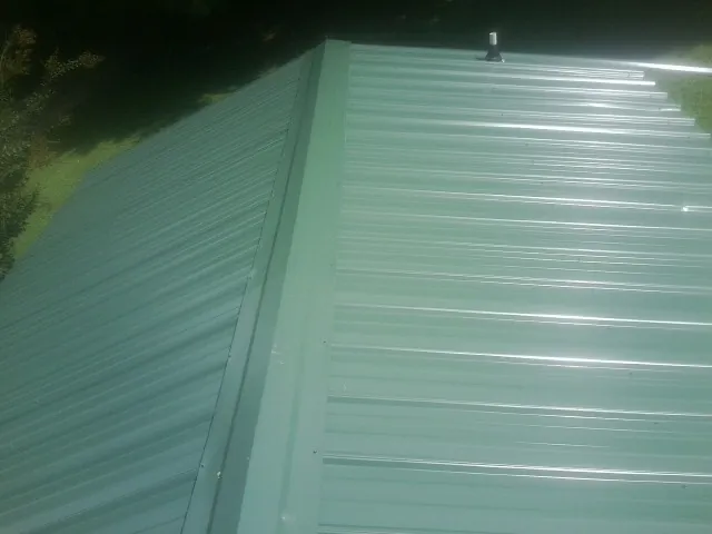 New green metal panels meeting at the ridge of a roof — Flat Roof Repair work by our crew in Saint Bonifacius