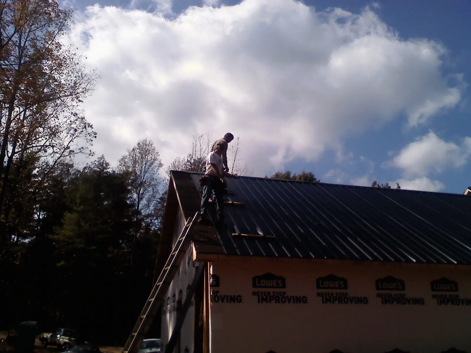 Roofer fastening dark metal panels high against a cloudy sky, from a Roof Inspection job in Saint Bonifacius
