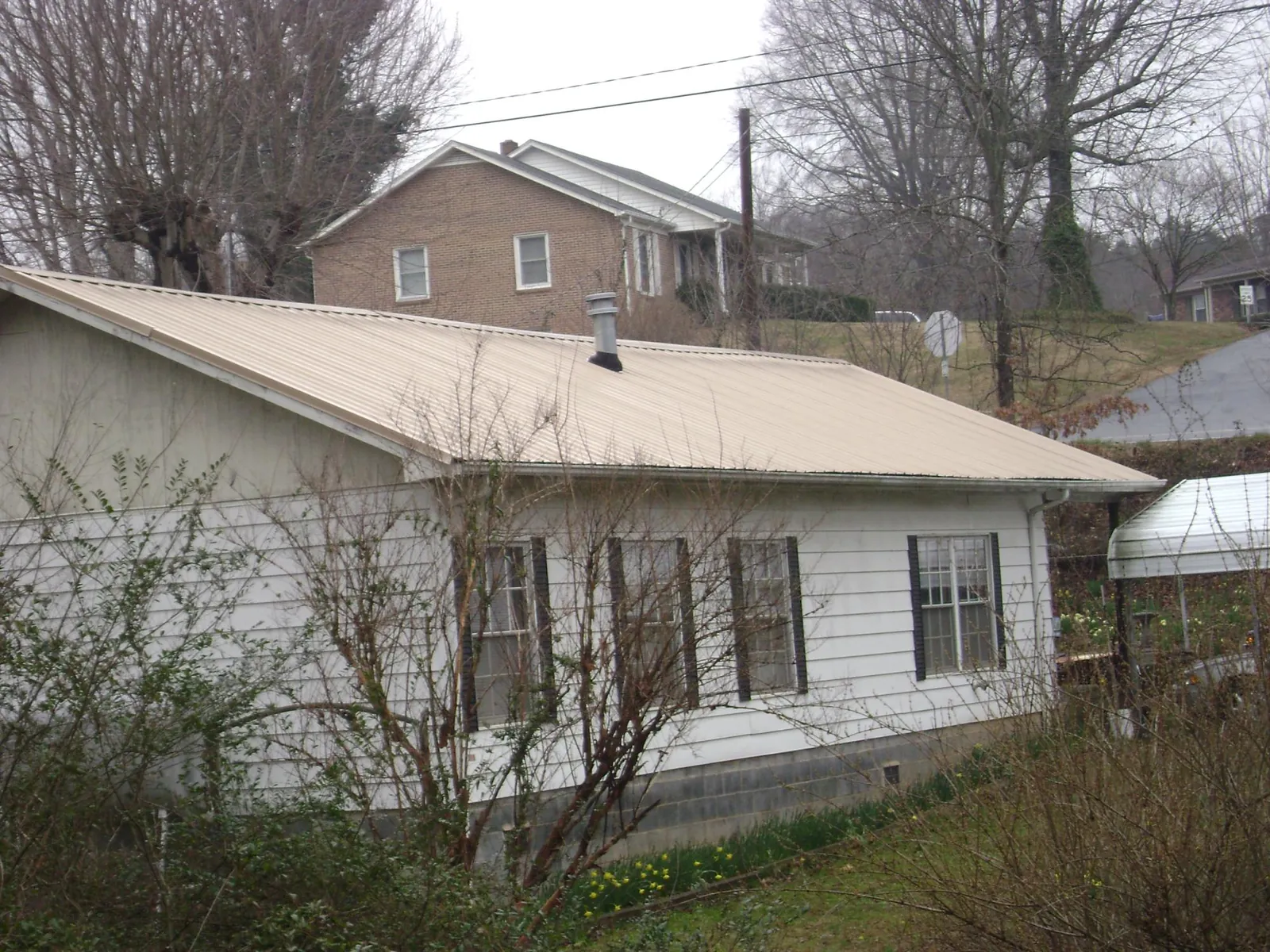 Tan metal roof on a white sided house set into a hillside — Commercial Roofing by Roofing Brothers in Saint Bonifacius