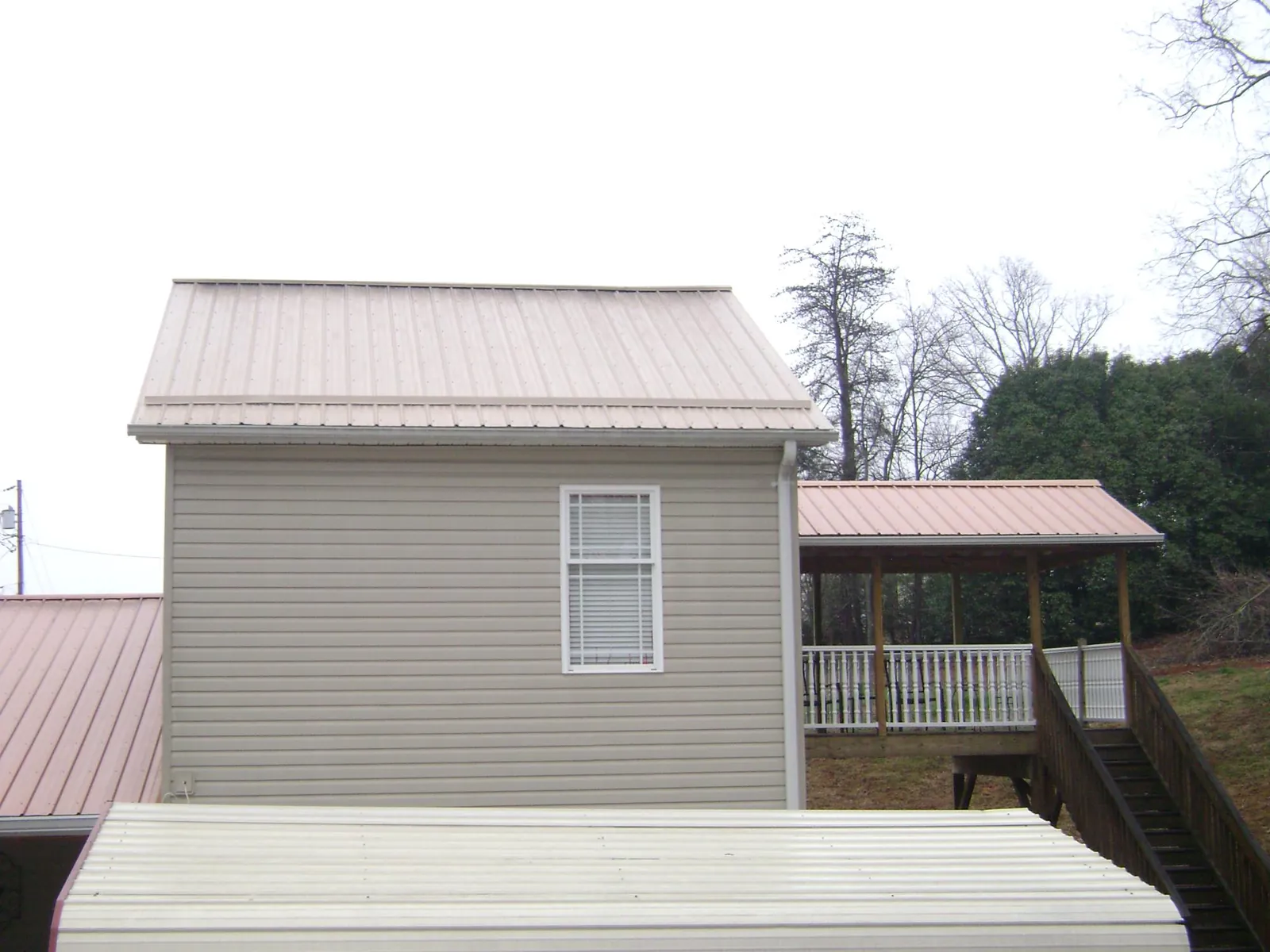 Tan metal roofs on a two story addition and attached porch, from a Roof Replacement job in Saint Bonifacius