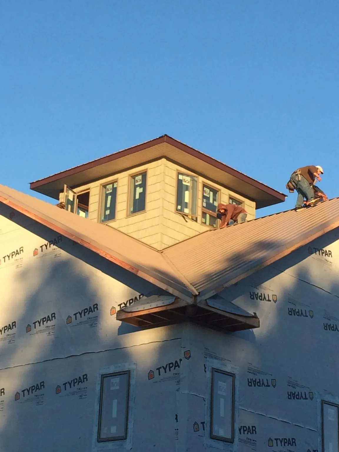 Roofers working around a rooftop cupola on a new metal roof at sunset in Saint Bonifacius